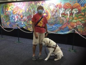 Lindy and Comet standing in front of a 6.5m quilted wall hanging decorated with brightly coloured Australian symbols
