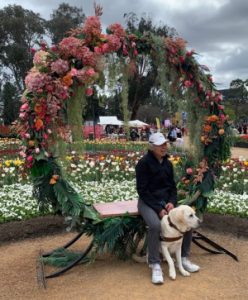 Lindy sitting with Comet sitting between her legs under an arch of flowers at Floriade
