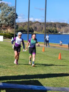 Lindy and Simone running on grass in front of Lake Burley Griffin
